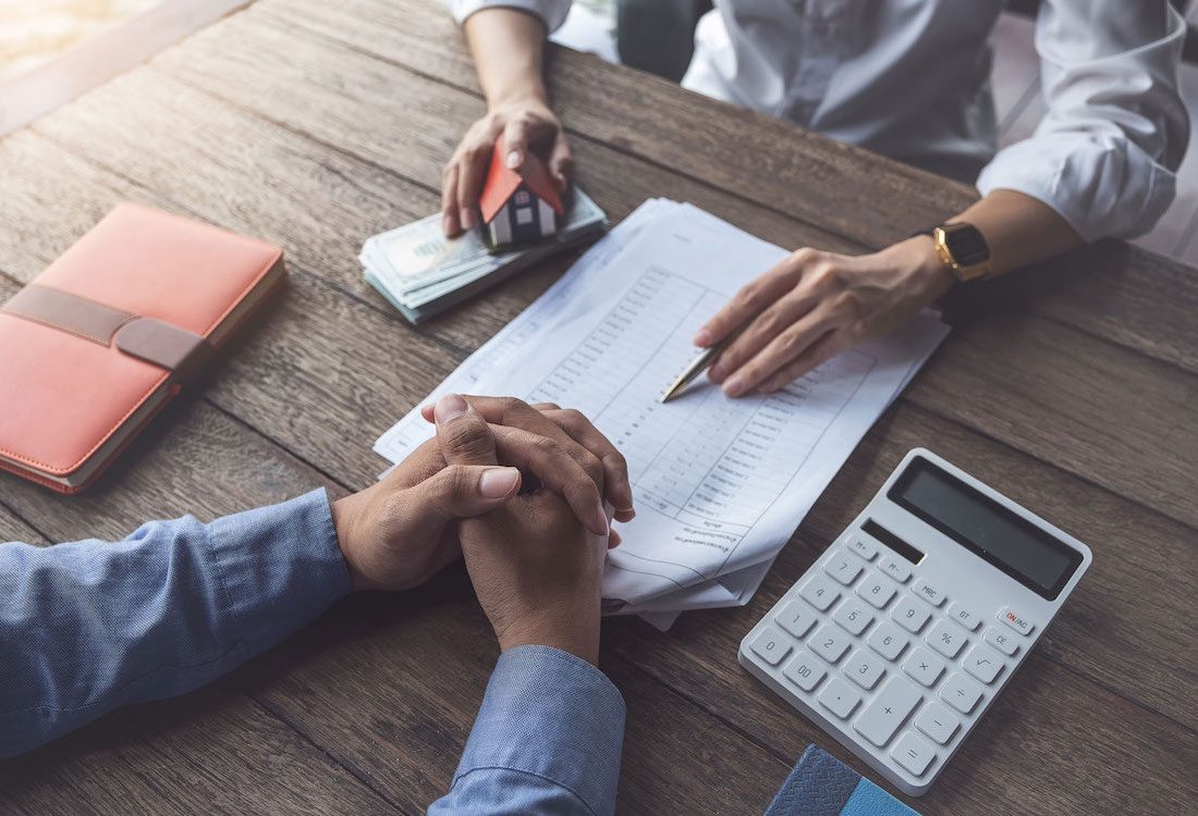 Loan agreement, real estate agent or bank officer describes the loan interest to the customer, along with loan documents with a home-style pen and a replica money on a wooden table.