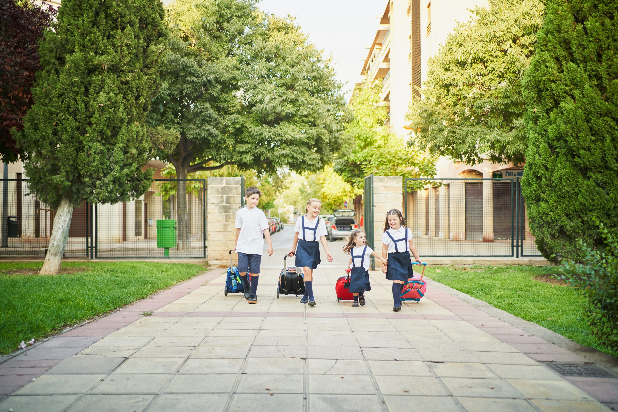 Unrecognizable spanish school kids riding her wheeled backpack to go class