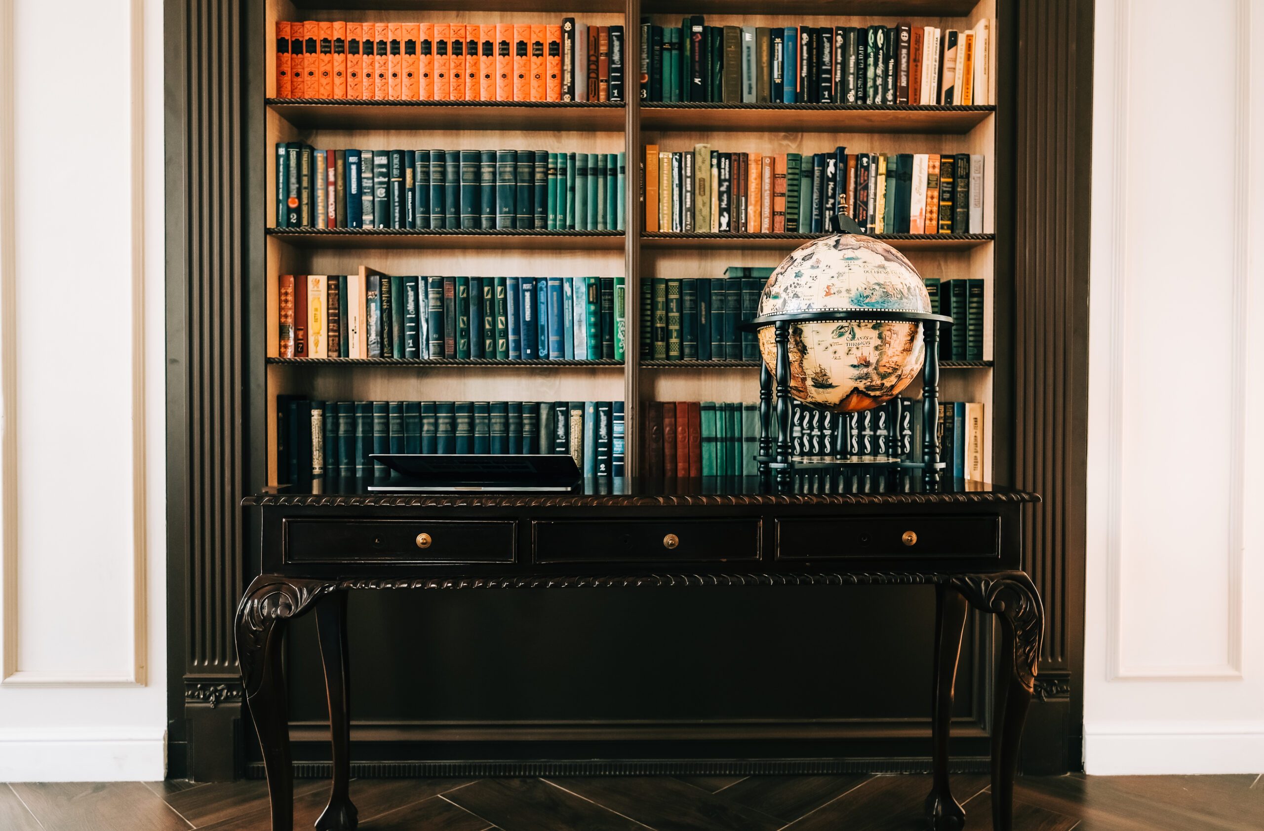 Big wooden vintage globe in a table near bookshelf in library.