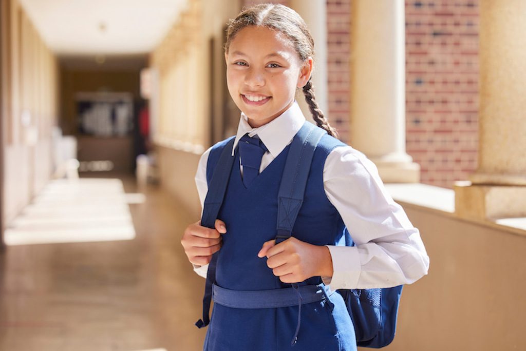 Education, school and portrait girl in a uniform with a backpack standing in the hallway for class.